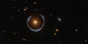 Obraz odległej niebieskiej galaktyki zniekształcony przez efekt soczewkowanie grawitacyjnego bliższej galaktyki czerwonej.
