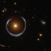 Obraz odległej niebieskiej galaktyki zniekształcony przez efekt soczewkowania grawitacyjnego bliższej galaktyki czerwonej.
